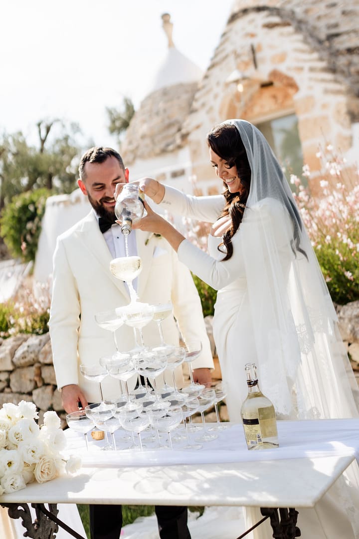 Couple pouring champagne on champagne tower during outdoor wedding reception